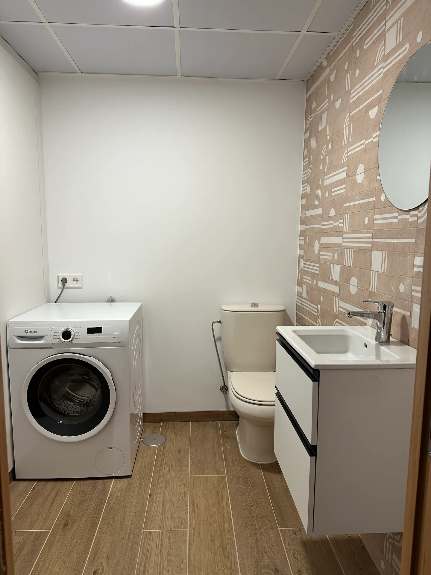 Aseo con inodoro, lavabo sobre mueble, espejo redondo y lavadora