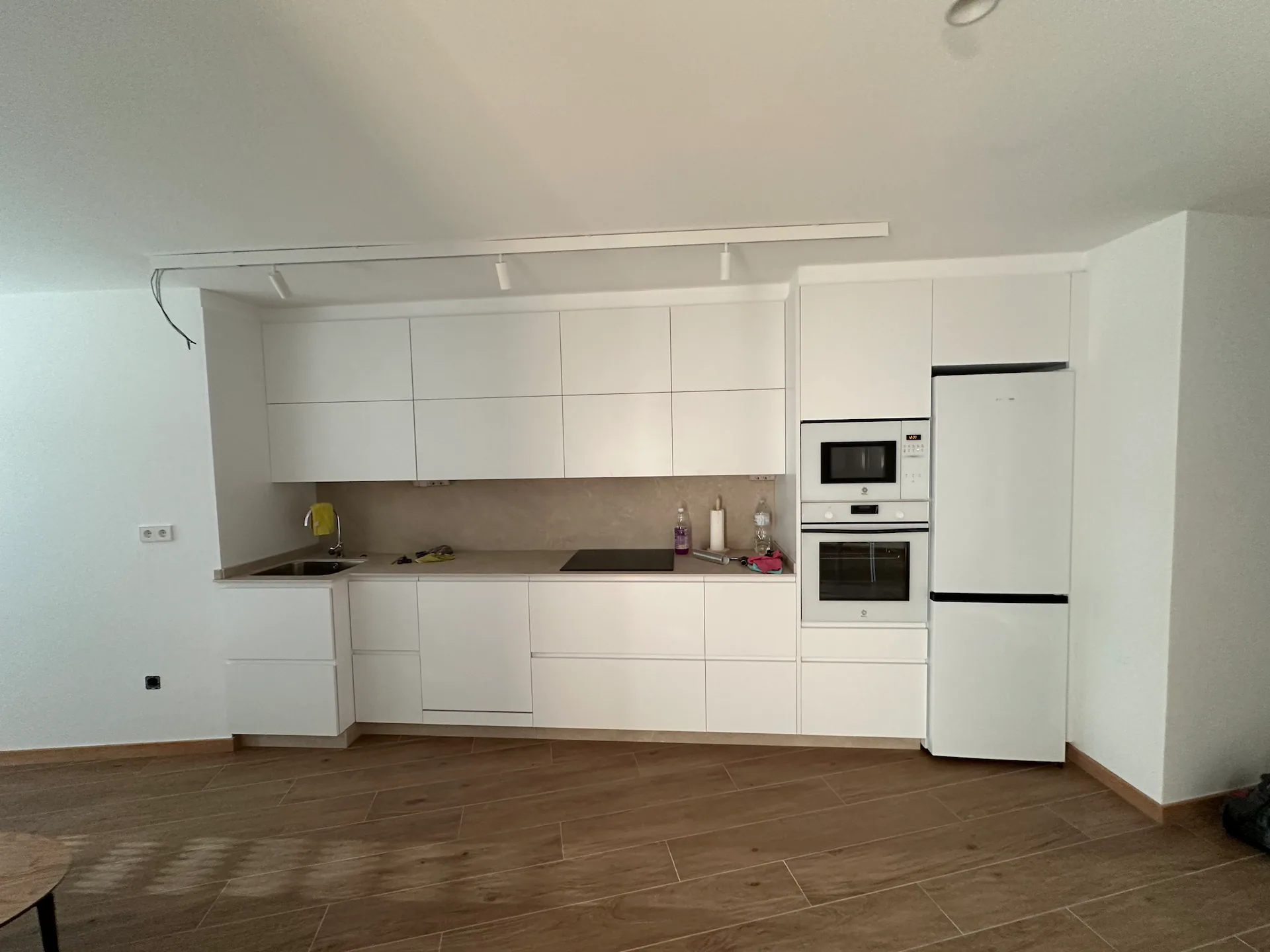 Cocina abierta en blanco con placa de inducción, horno y microondas empotrados, frigorífico y amplio almacenaje