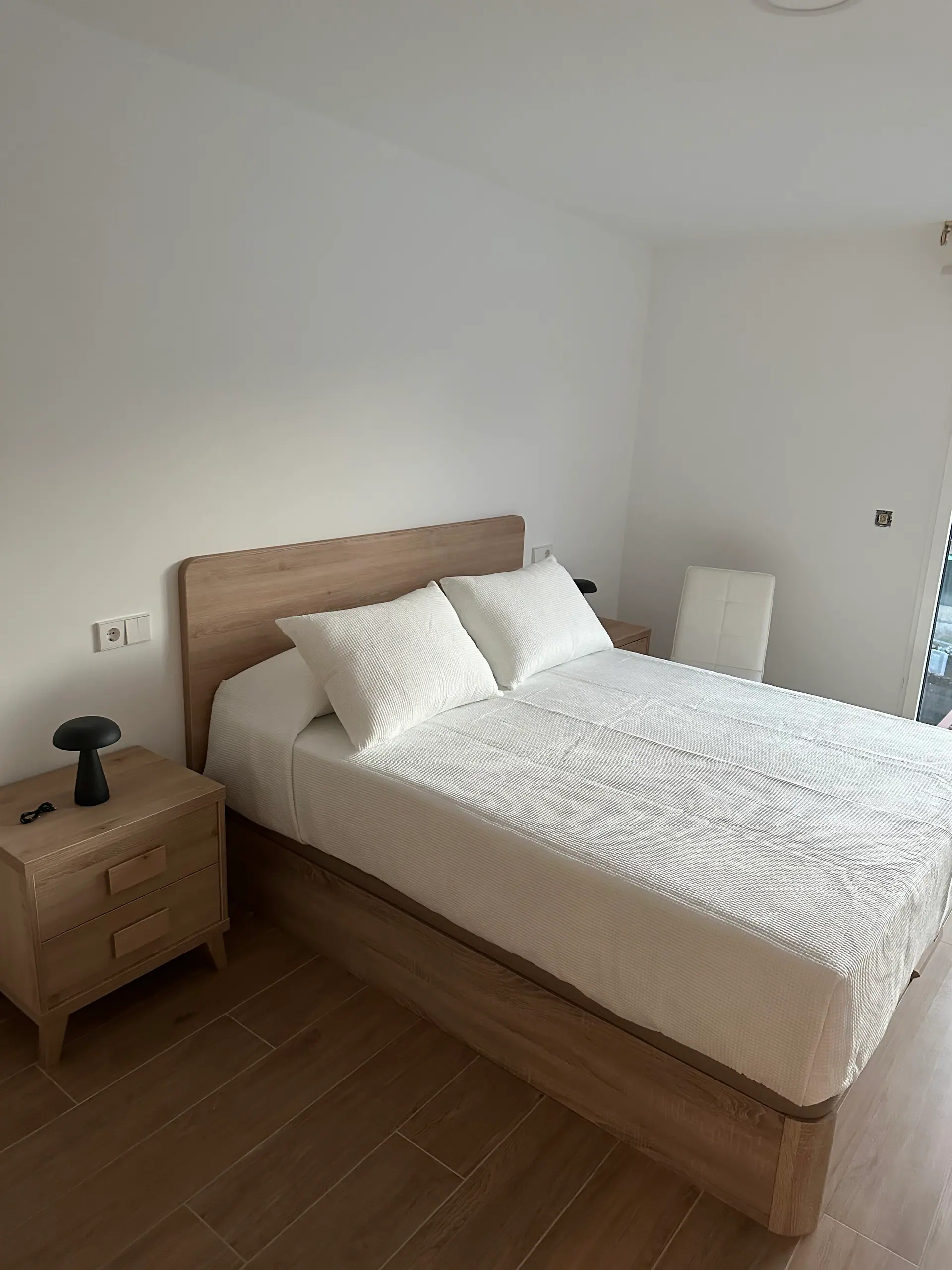 Dormitorio principal con cama de matrimonio, cabecero de madera clara, mesillas a juego y lámpara de sobremesa negra