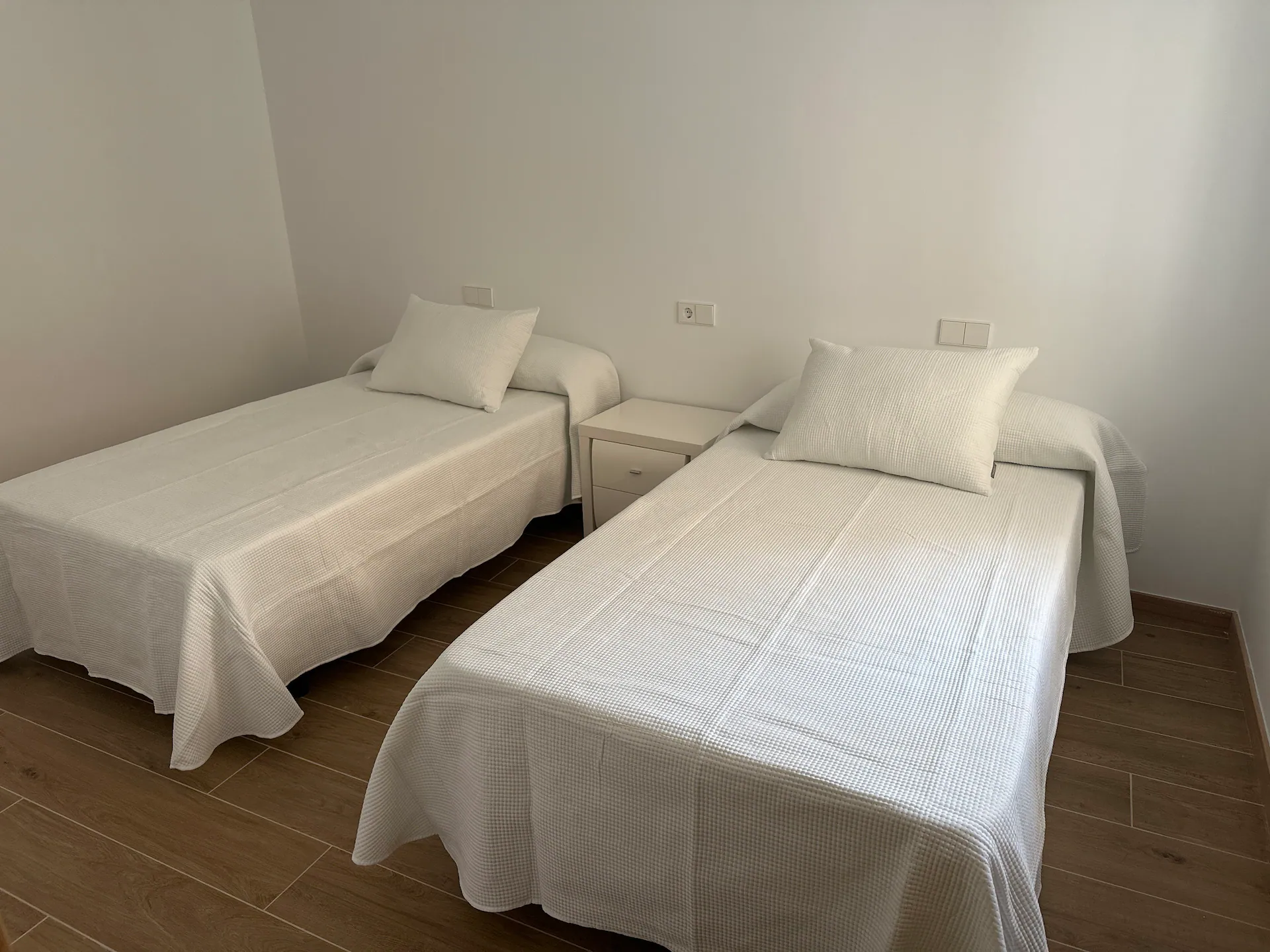 Segundo dormitorio con dos camas individuales vestidas en blanco y una mesilla compartida