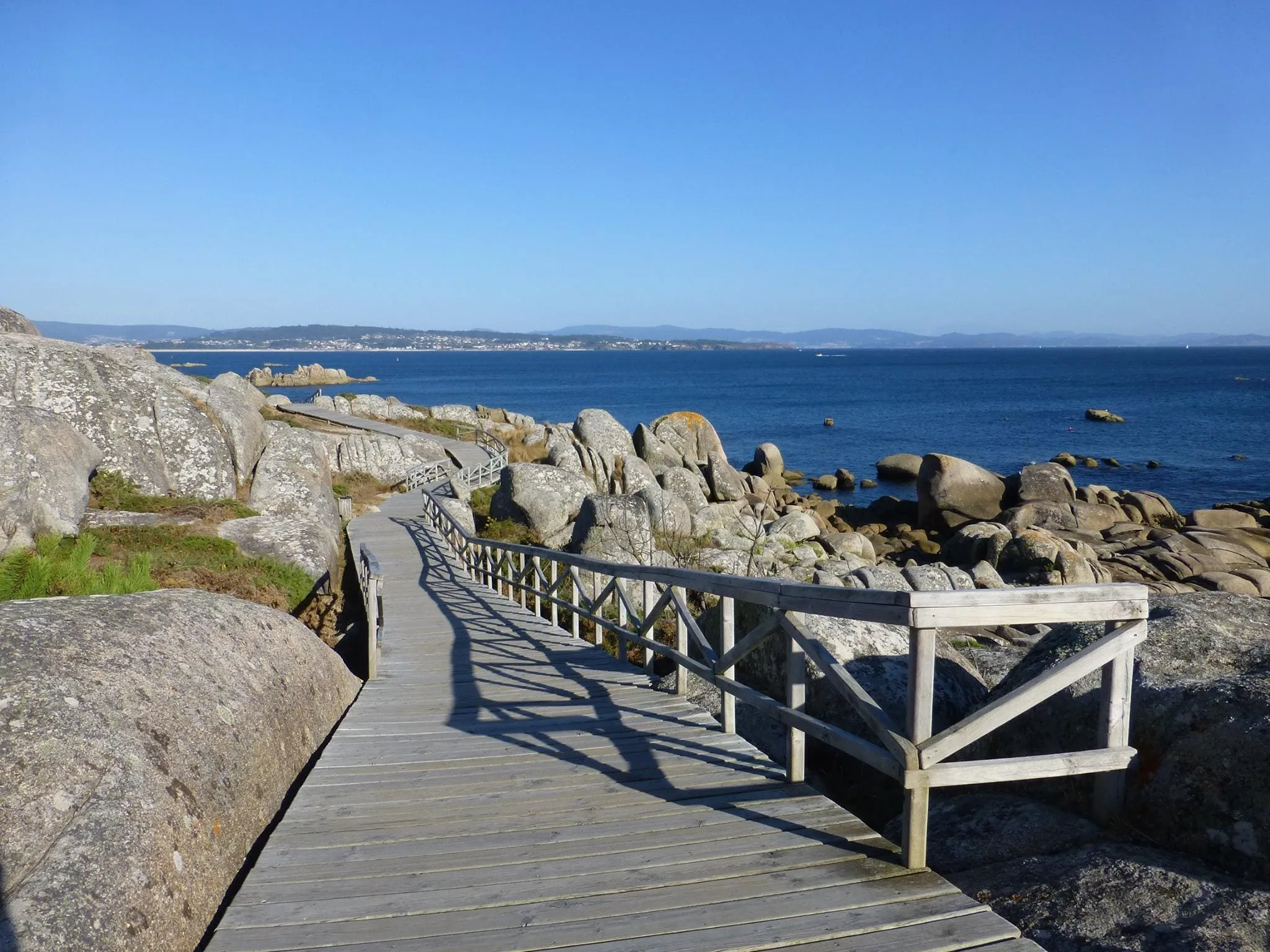 Pasarela de madera sobre las rocas de granito, con la ría de Arousa al fondo