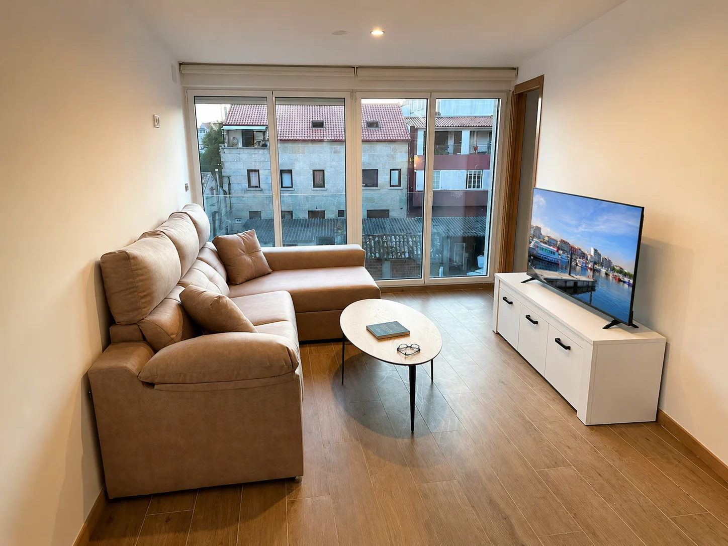 Salón del apartamento con sofá chaise longue y ventanal sobre los tejados de piedra del casco antiguo de O Grove