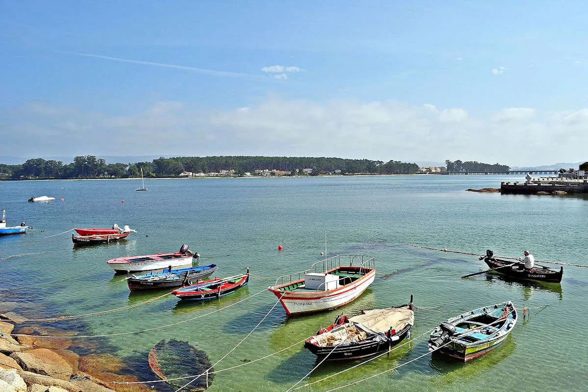 Barcas de pesca fondeadas en agua turquesa, con el puente de A Toxa al fondo